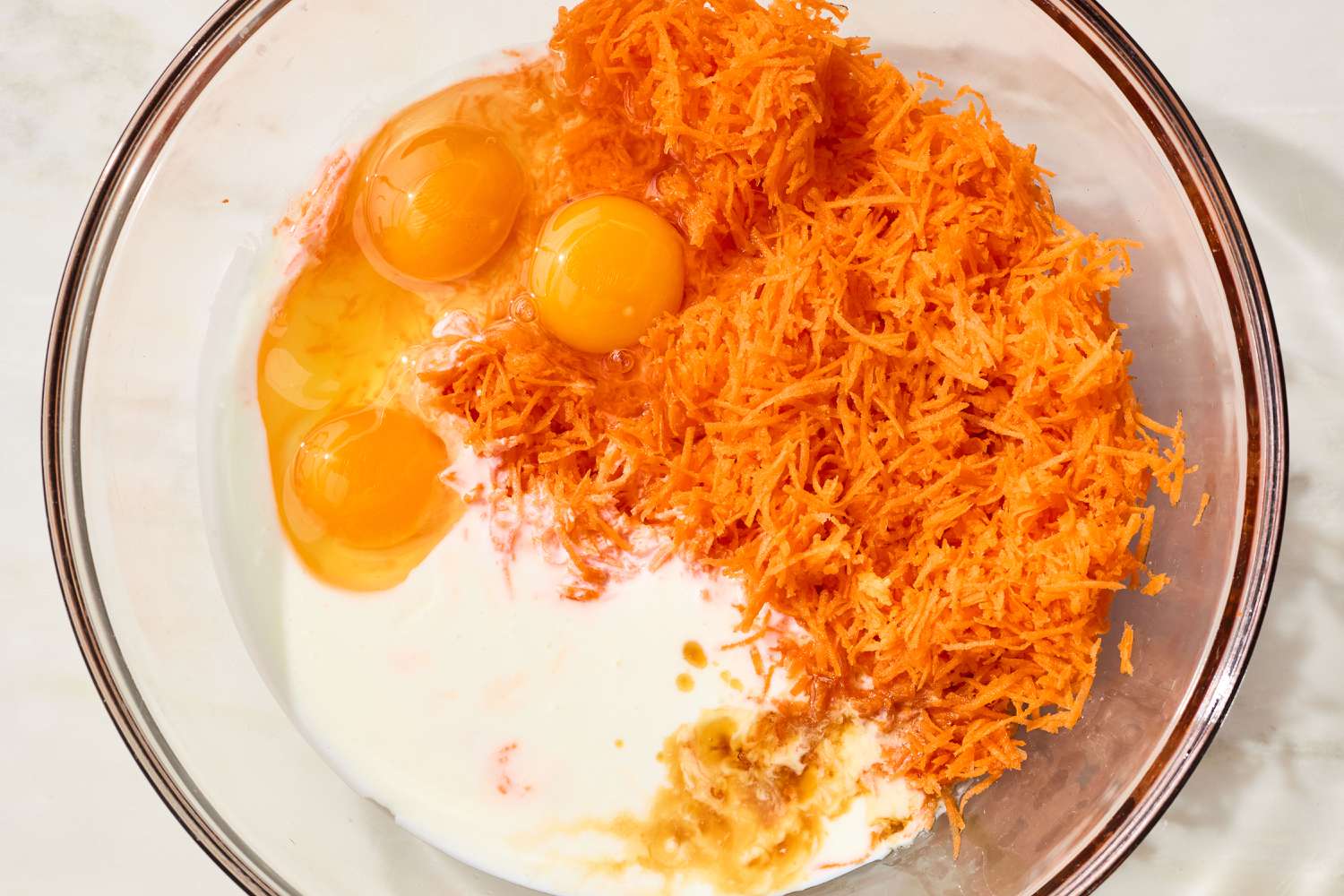 overhead view of a large mixing bowl with grated carrots, eggs, and other wet ingredients for carrot cake waffles recipe