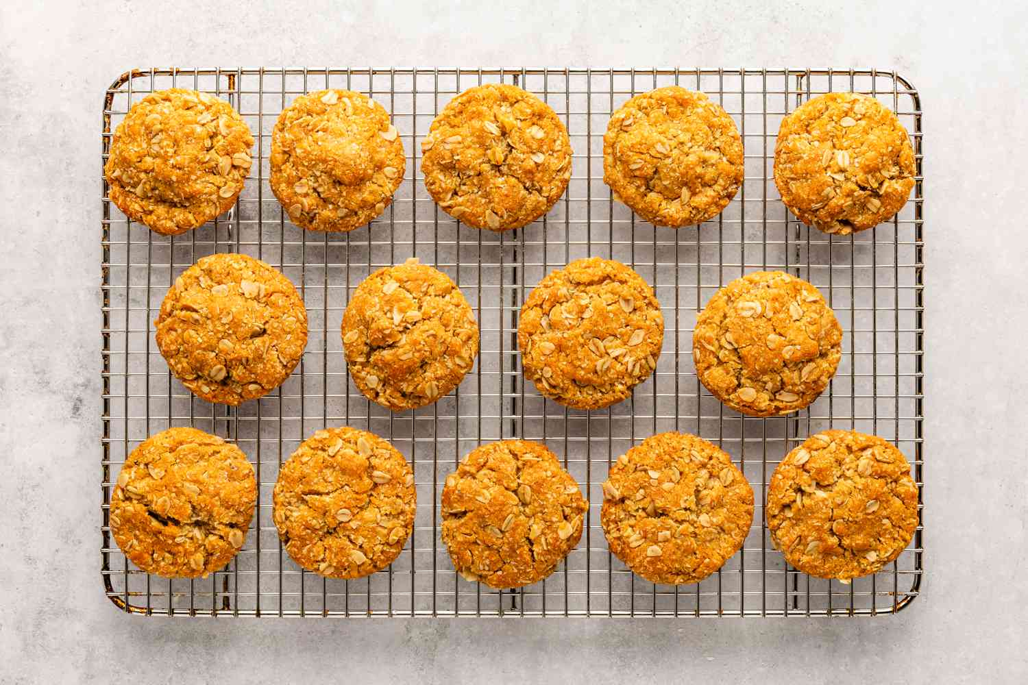 Fourteen baked cookies for the Anzac Biscuits recipe cooling on a cooling rack