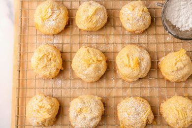 Overhead view of potato chip cookies on a cooling rack over parchment paper next to a owl of powdered sugar