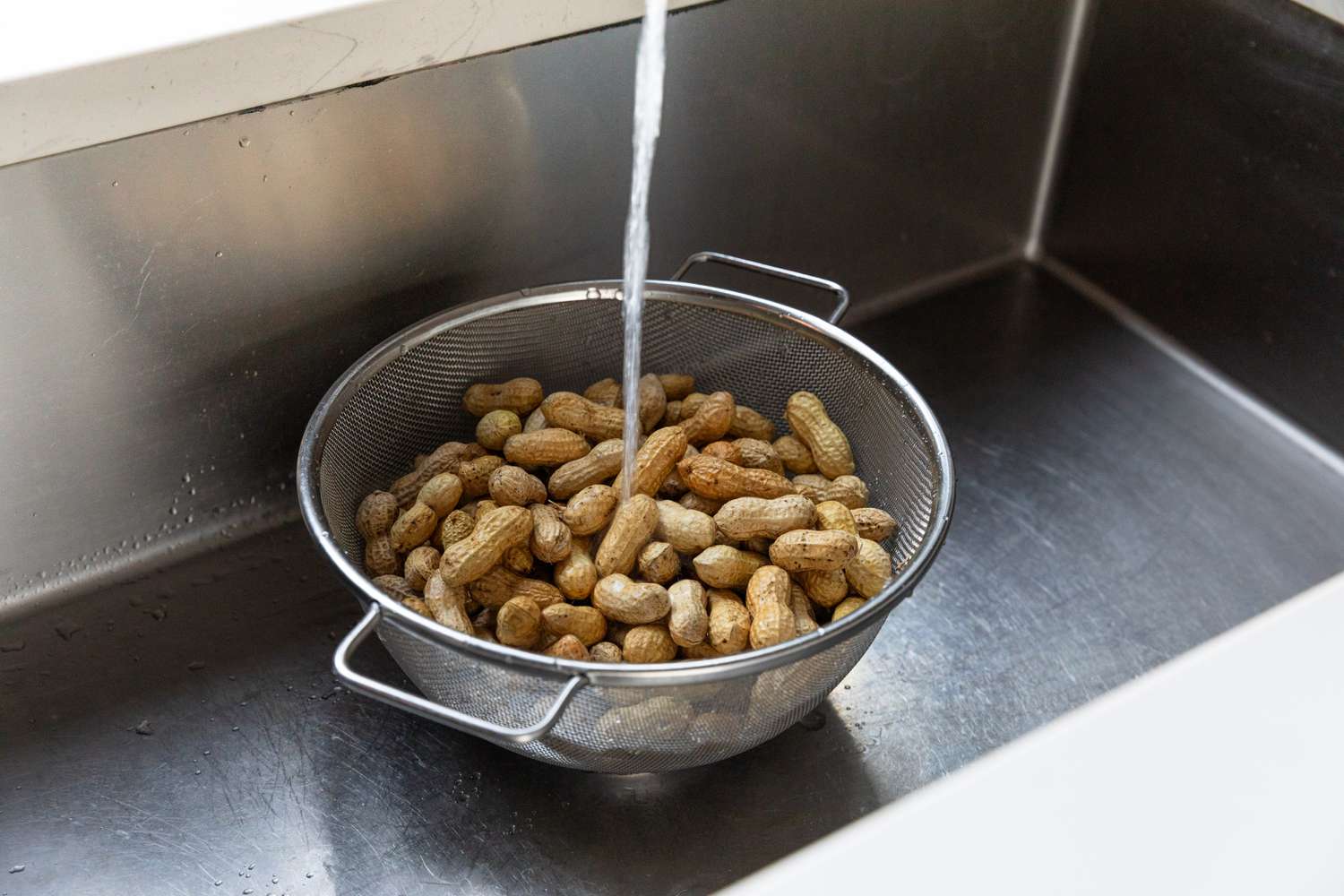 Rinsing a colander of raw peanuts in their shells under a sink