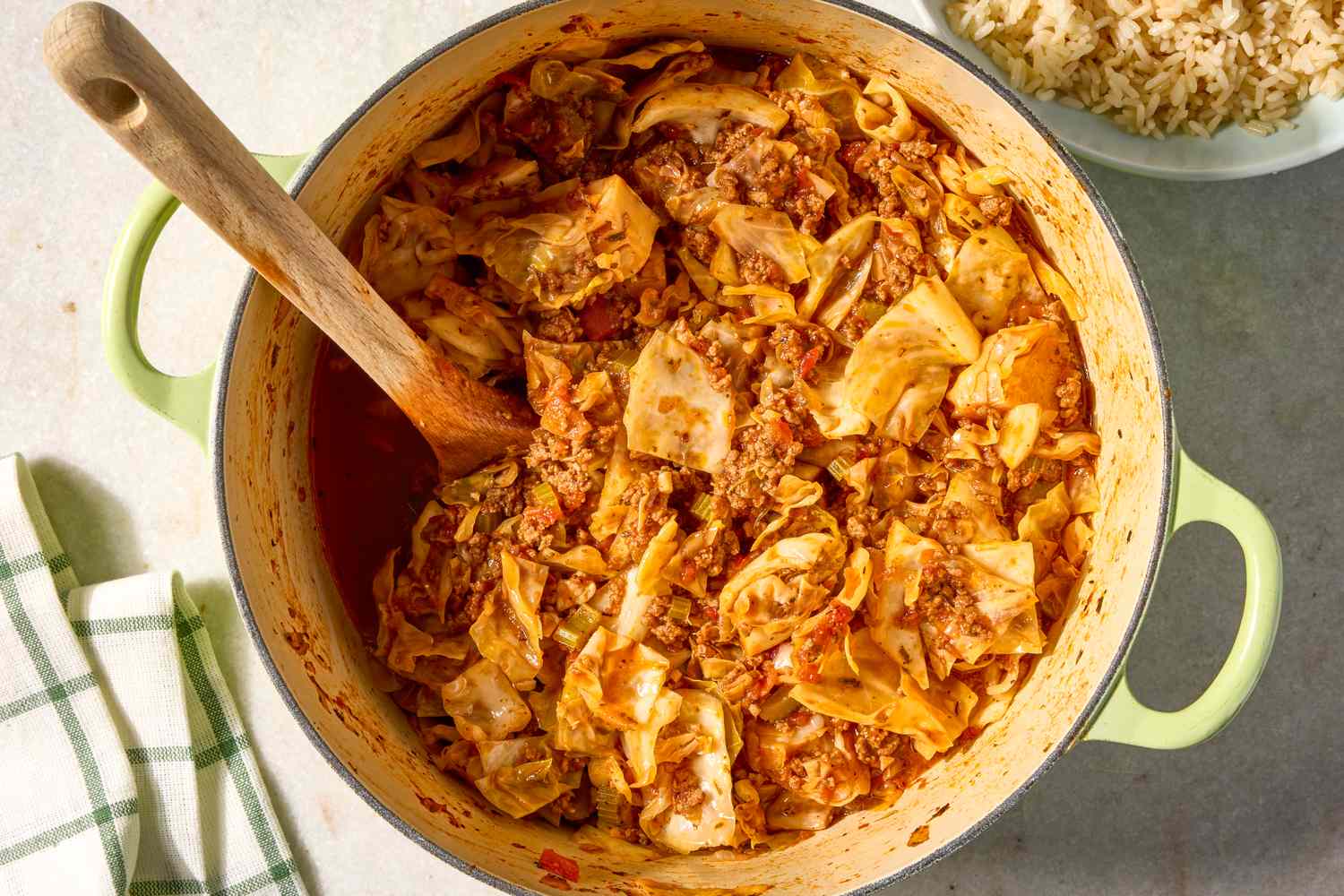 A pot of cooked ground beef and cabbage with a wooden spoon stirring it