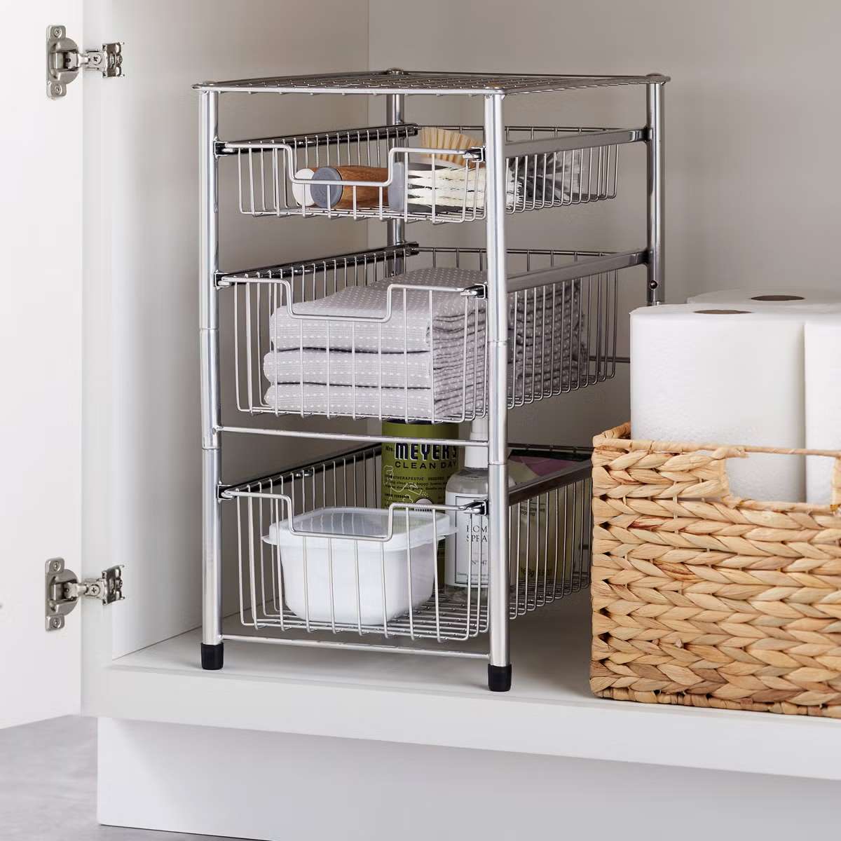 Wire pullout cabinet organizer in a cupboard with items like towels and a basket of supplies