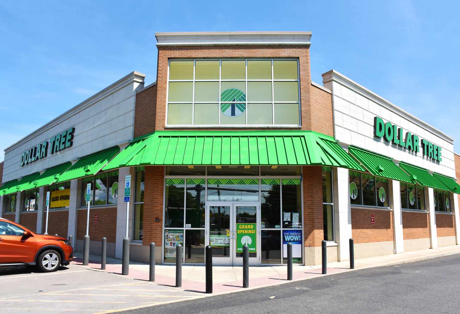 Entrance of a Dollar Tree store with visible signage and green awning parked orange car to the left