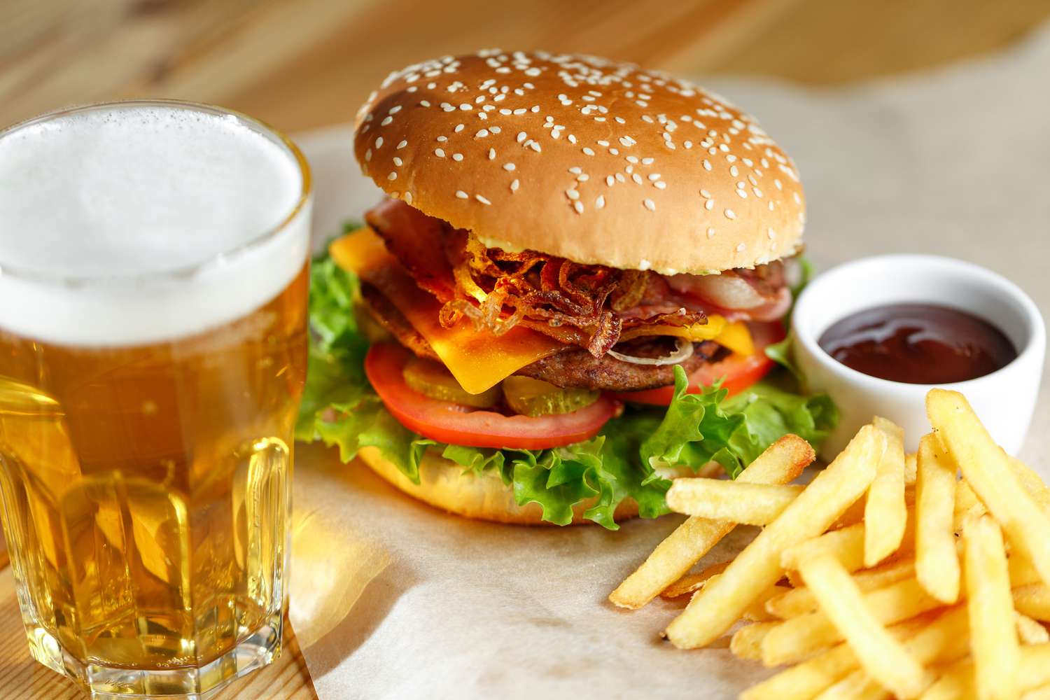 Hamburger with lettuce, cheese, tomato, and bacon, served with french fries, ketchup, and a glass of beer