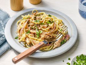 Linguine with tuna and capers on a plate at a table setting with a bowl of parsley, a denim table napkin, salt and pepper shakers, and a glass of water