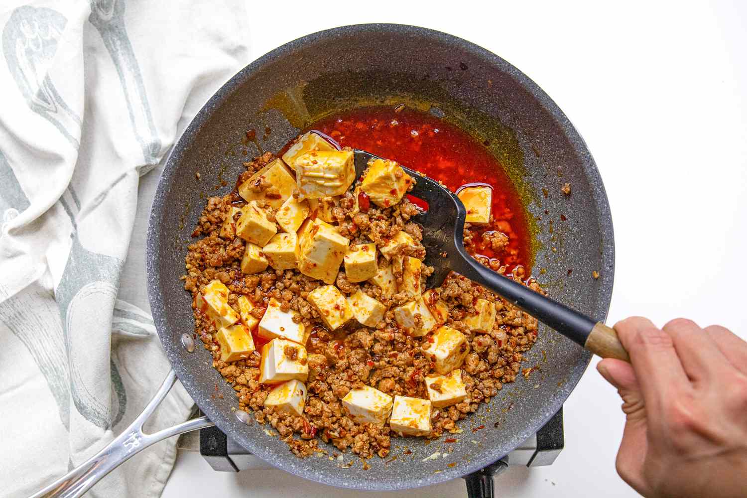 Mapo Tofu Ingredients Stirred Together Using a Slotted Spatula After Cornstarch Slurry Was Added to the Pan on a Portable Burner Next to a White Kitchen Towel