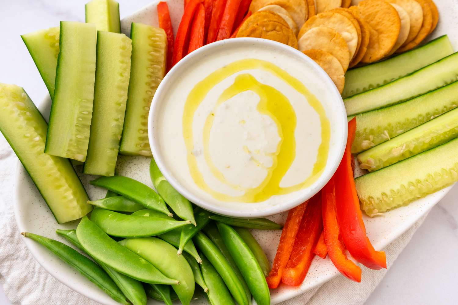 A plate with fresh cut vegetables pita slices and a bowl of dip garnished with oil