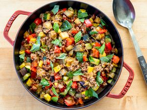A skillet containing a cooked dish of diced vegetables and ground beef, garnished with fresh basil