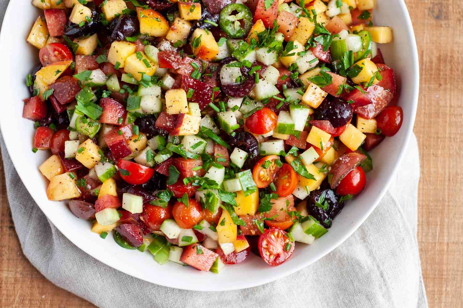 Peach, plum, cherry, and tomato salad in a serving bowl with a white linen underneath.