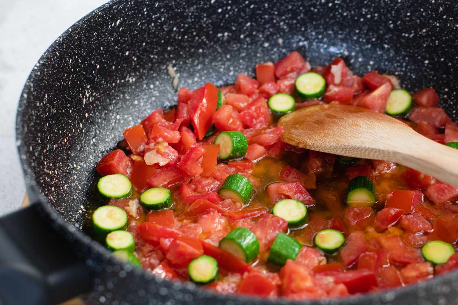 A wooden spoon stirring primavera sauce in a skillet.