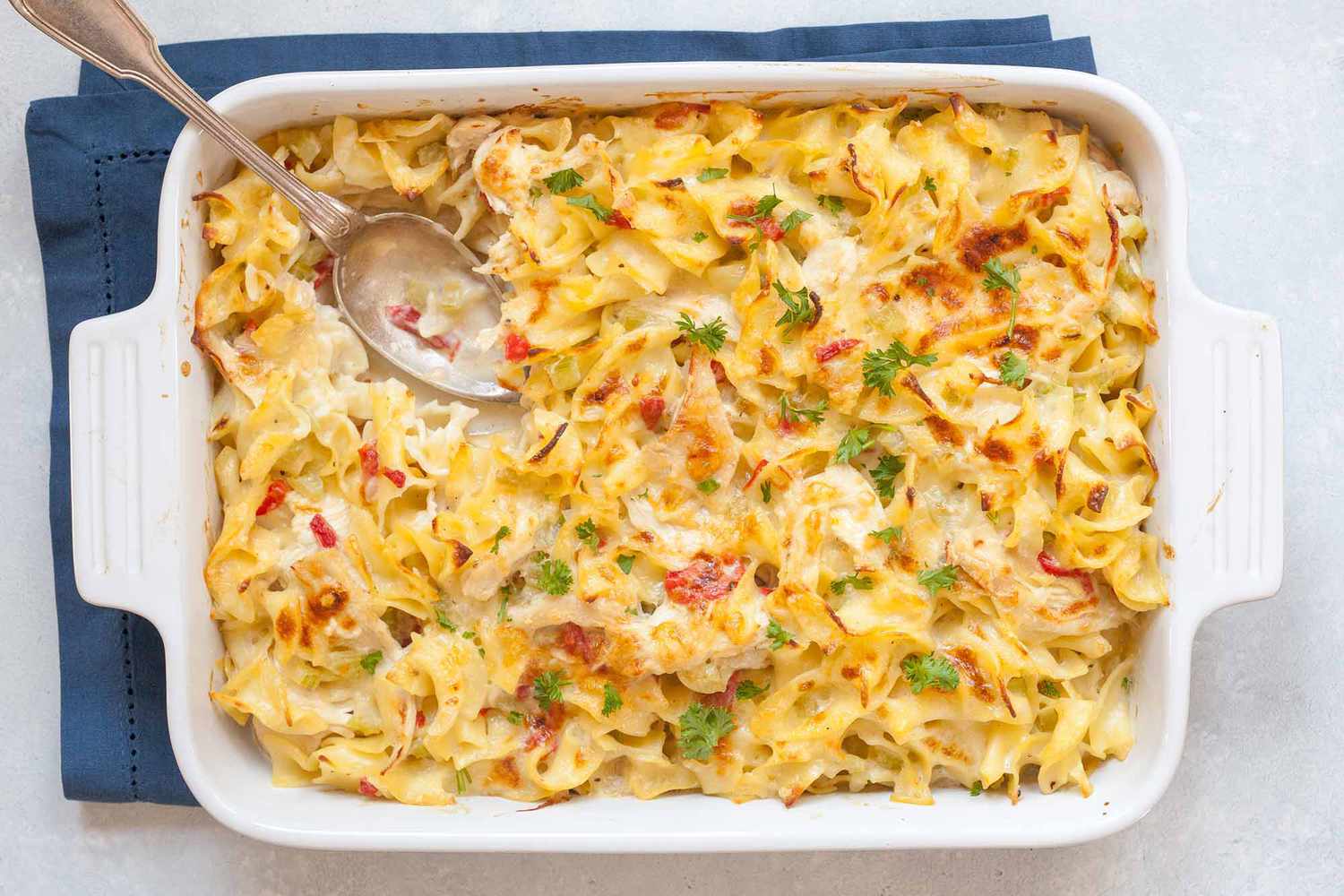 Creamy Chicken Noodle Casserole in a white baking dish with a silver spoon.