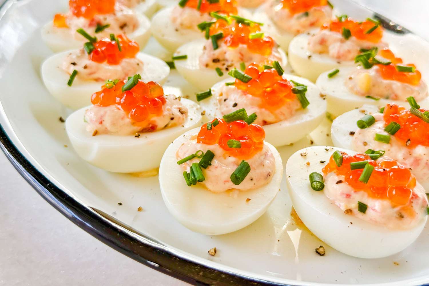 Deviled eggs topped with red caviar and chopped chives on a serving plate