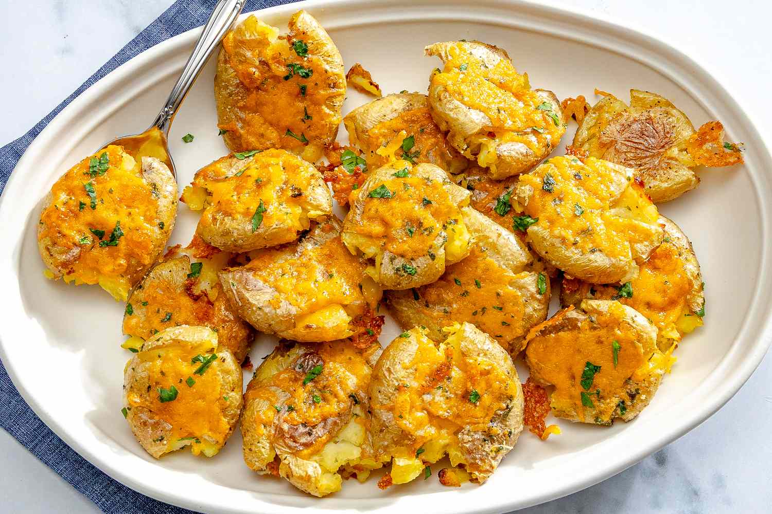 A dish of smashed potatoes topped with cheese and garnished with herbs