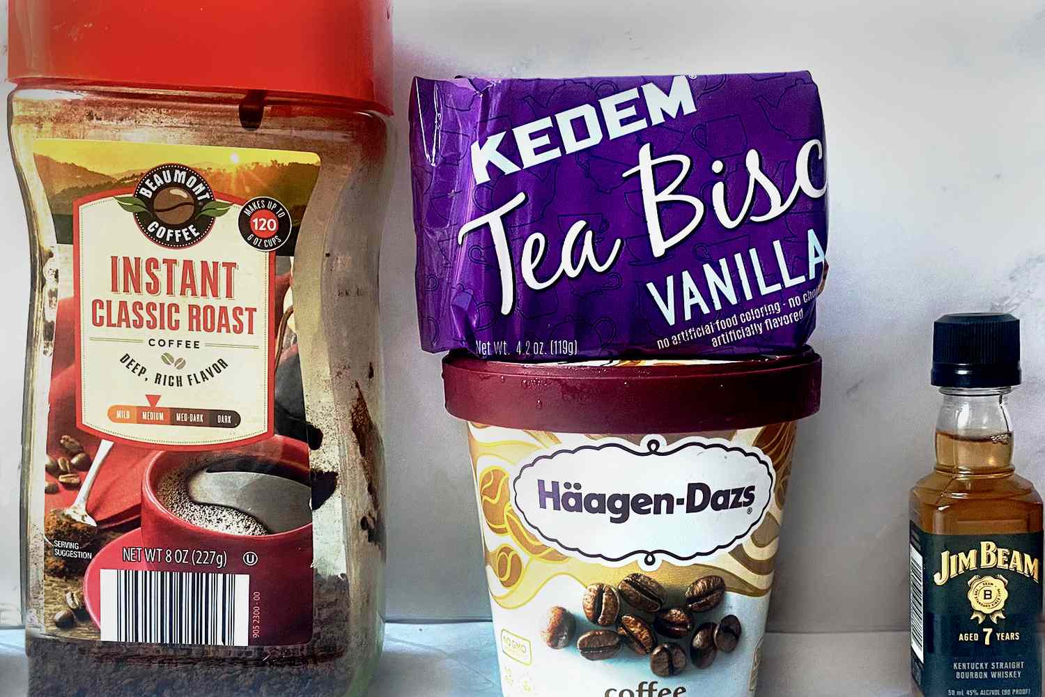 Ingredients including instant coffee, vanilla wafer biscuits, coffee ice cream, and a small bottle of bourbon on a table