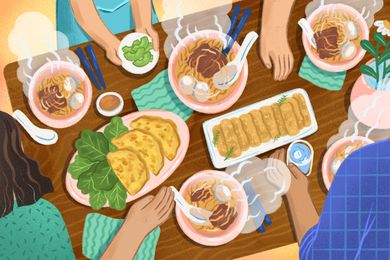 Family sitting down to dinner at a table with bowls of pho