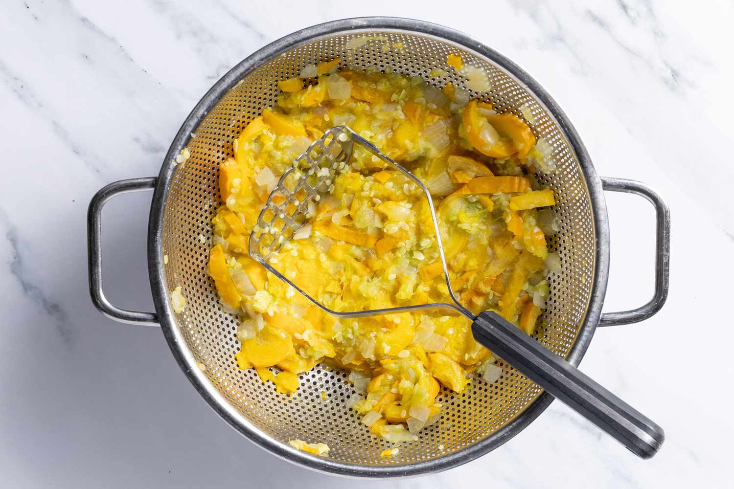 cooked onions and summer squash mashed together in the colander for southern summer squash casserole recipe