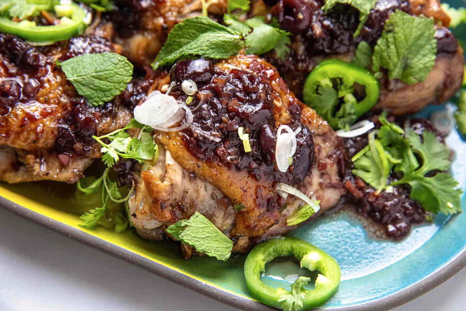 Sticky chicken with garnishes of herbs scallions and chili slices presented on a platter