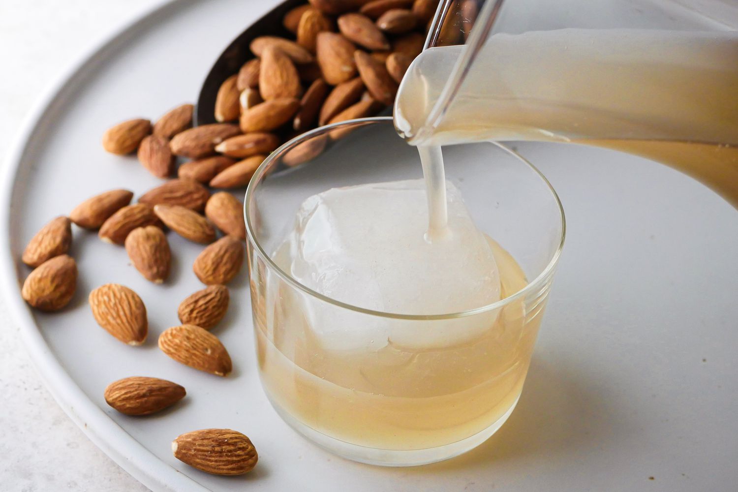 Pouring Orgeat, almond syrup for cocktails, into an ice filled glass with raw almonds next to it.