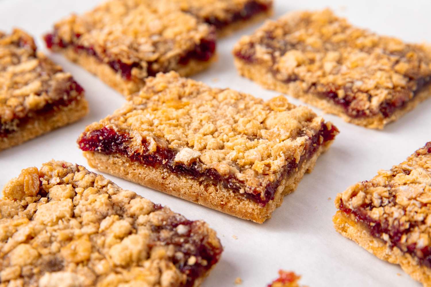 Raspberry jam bars arranged in rows on a light surface with a crumbly topping and layers visible