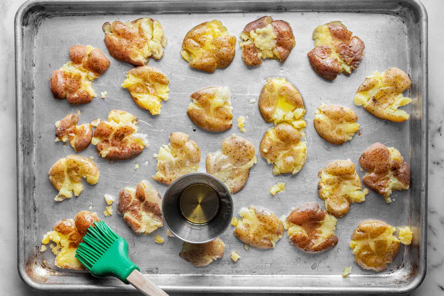 Smashed Potatoes Transferred onto a Baking Pan and Coated with Olive Oil Using a Basting Brush 