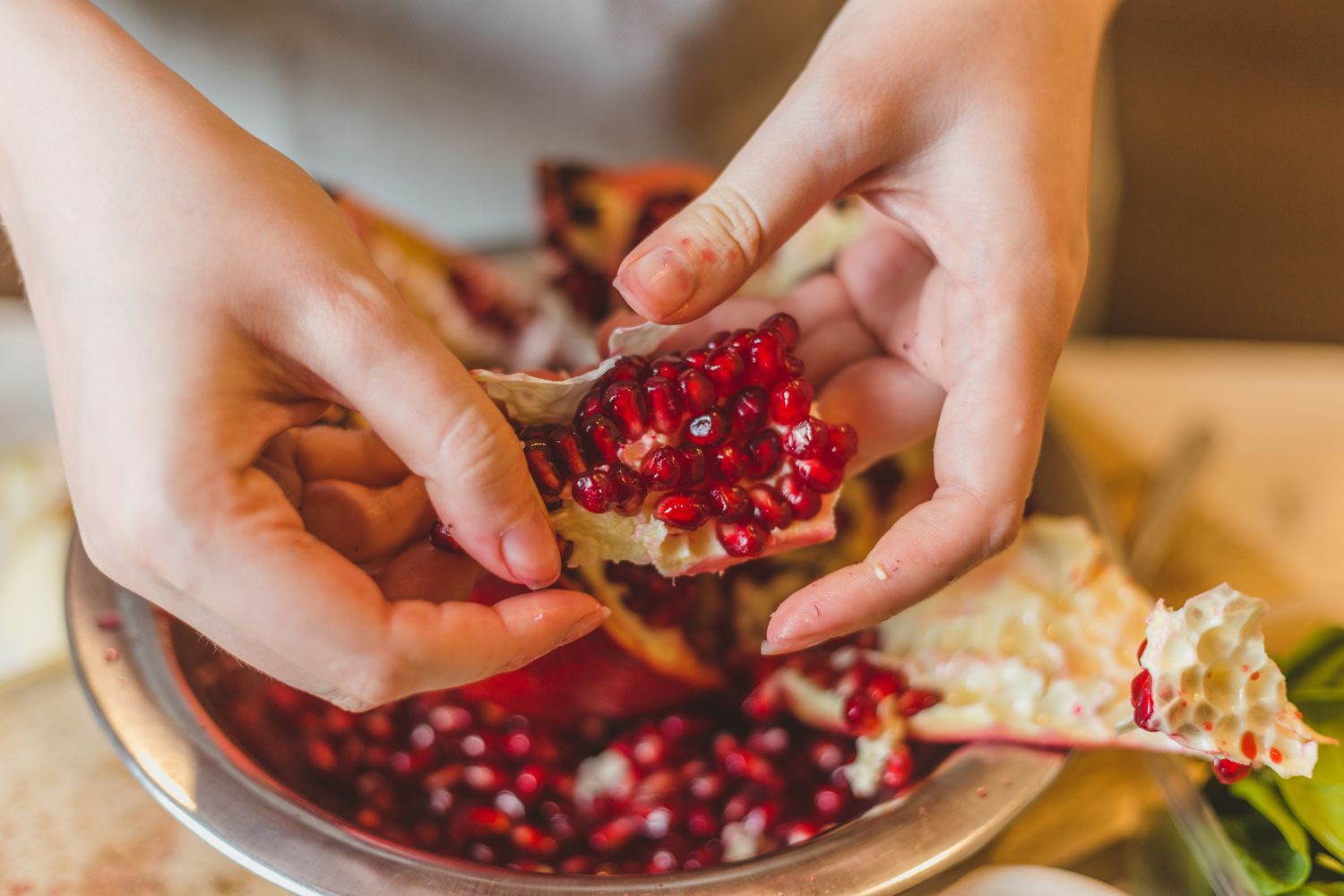 Hands removing pomegranate seeds from a pomegranate