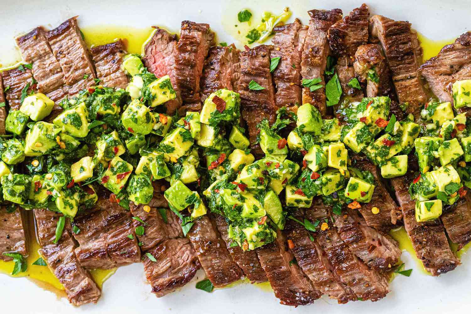 Quick and Easy weeknight skirt steak sliced across the grain and covered with avocado chimichurri on a white plate
