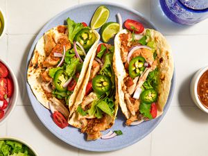 Plate of chicken tacos garnished with jalapeños, onions, and greens, served with lime wedges and salsa on the side