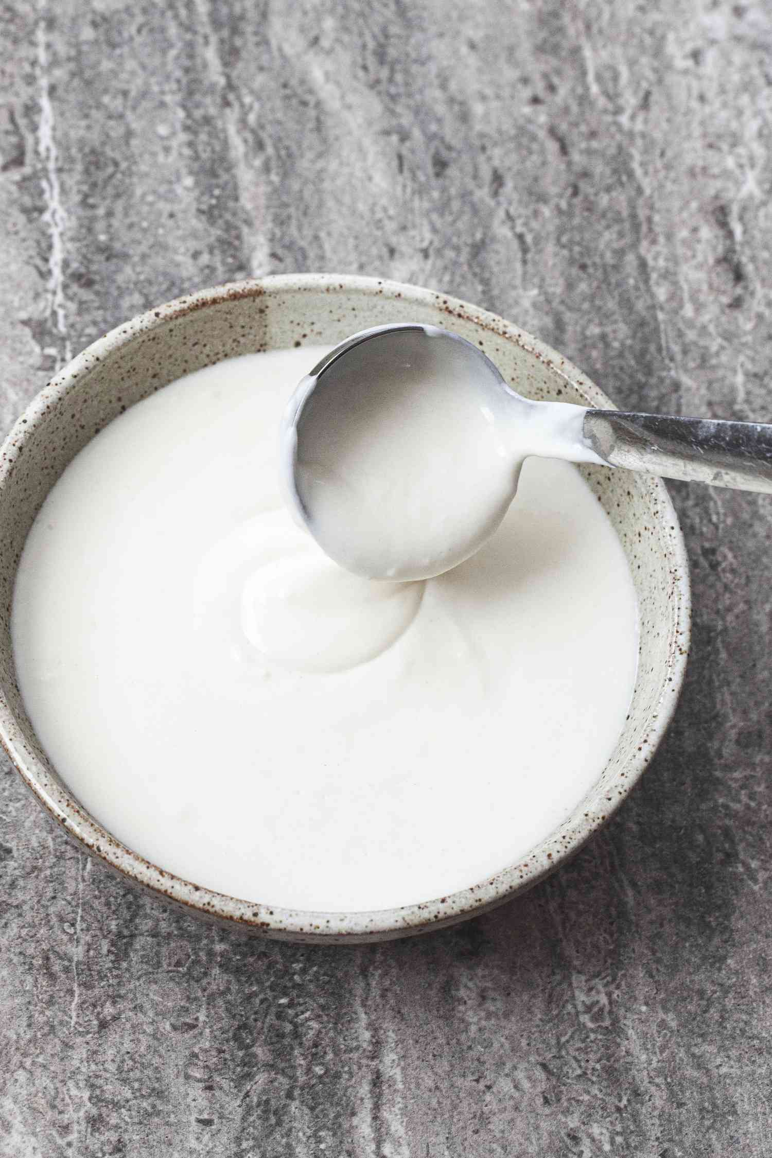 Basic béchamel sauce in a bowl with a small ladle dipping into the bowl.