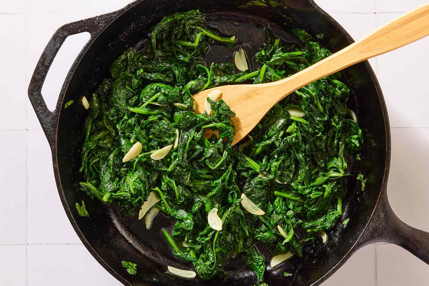 Sauted spinach with garlic in a cast iron skillet with a wooden spoon