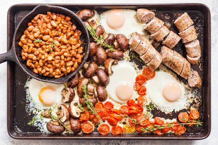Full English Breakfast on a Sheet Pan -- a pot of beans, cracked eggs, sausages, potatoes, and tomatoes
