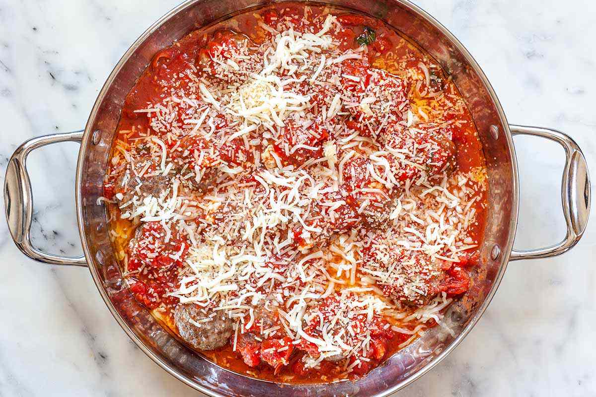 Mozzarella stuffed meatballs in a skillet with tomato sauce and cheese
