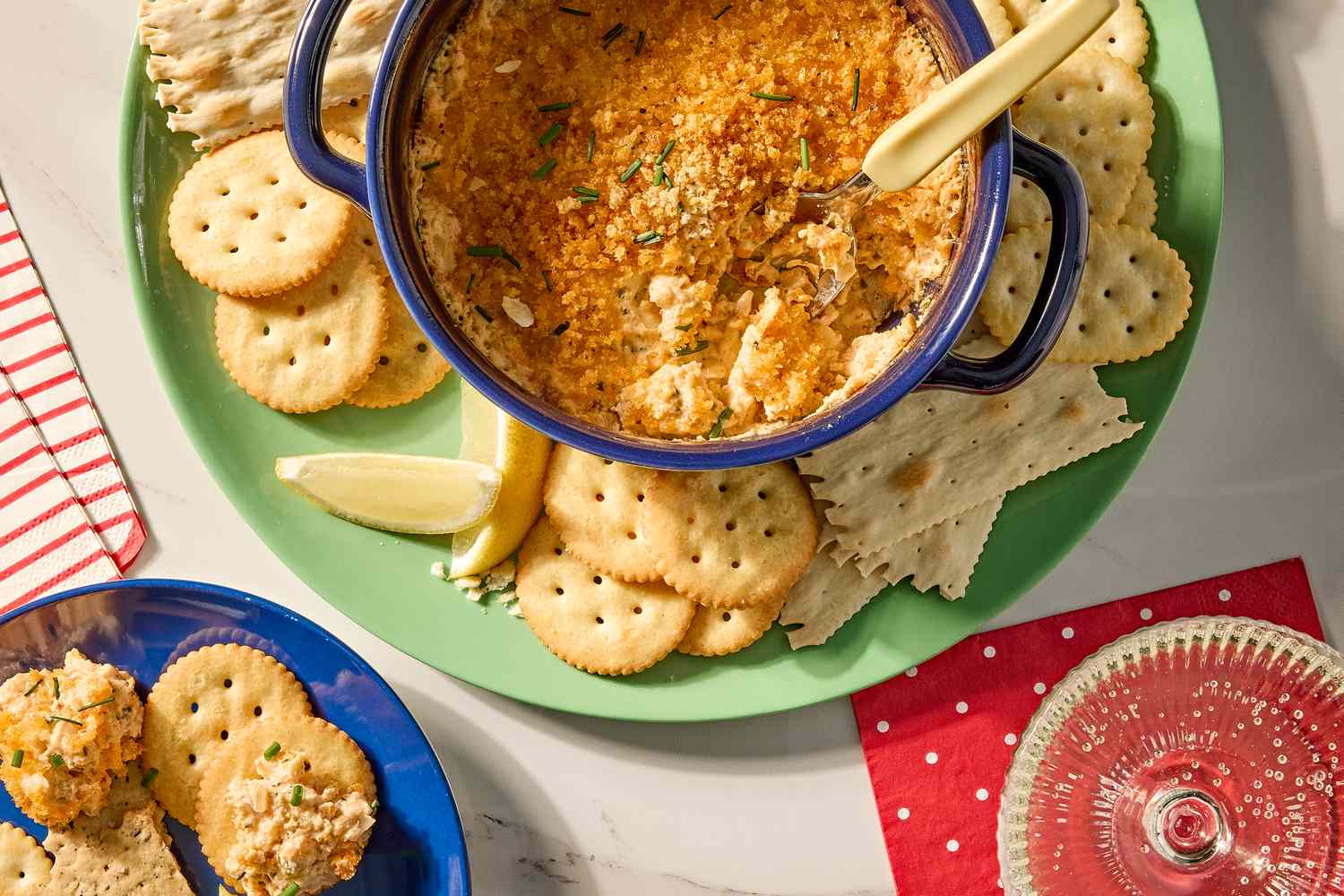 Baked seafood dip in a dish surrounded by crackers and lemon wedges on a table