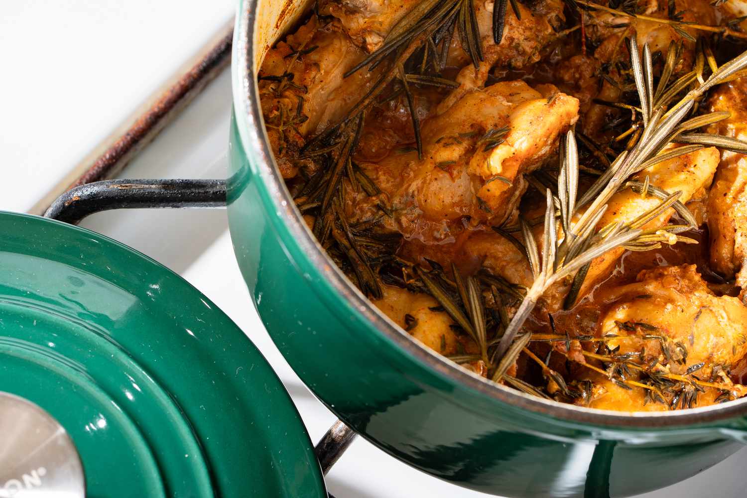 The green Dutch oven from ALDI with cooked chicken wings and a rosemary sprig inside
