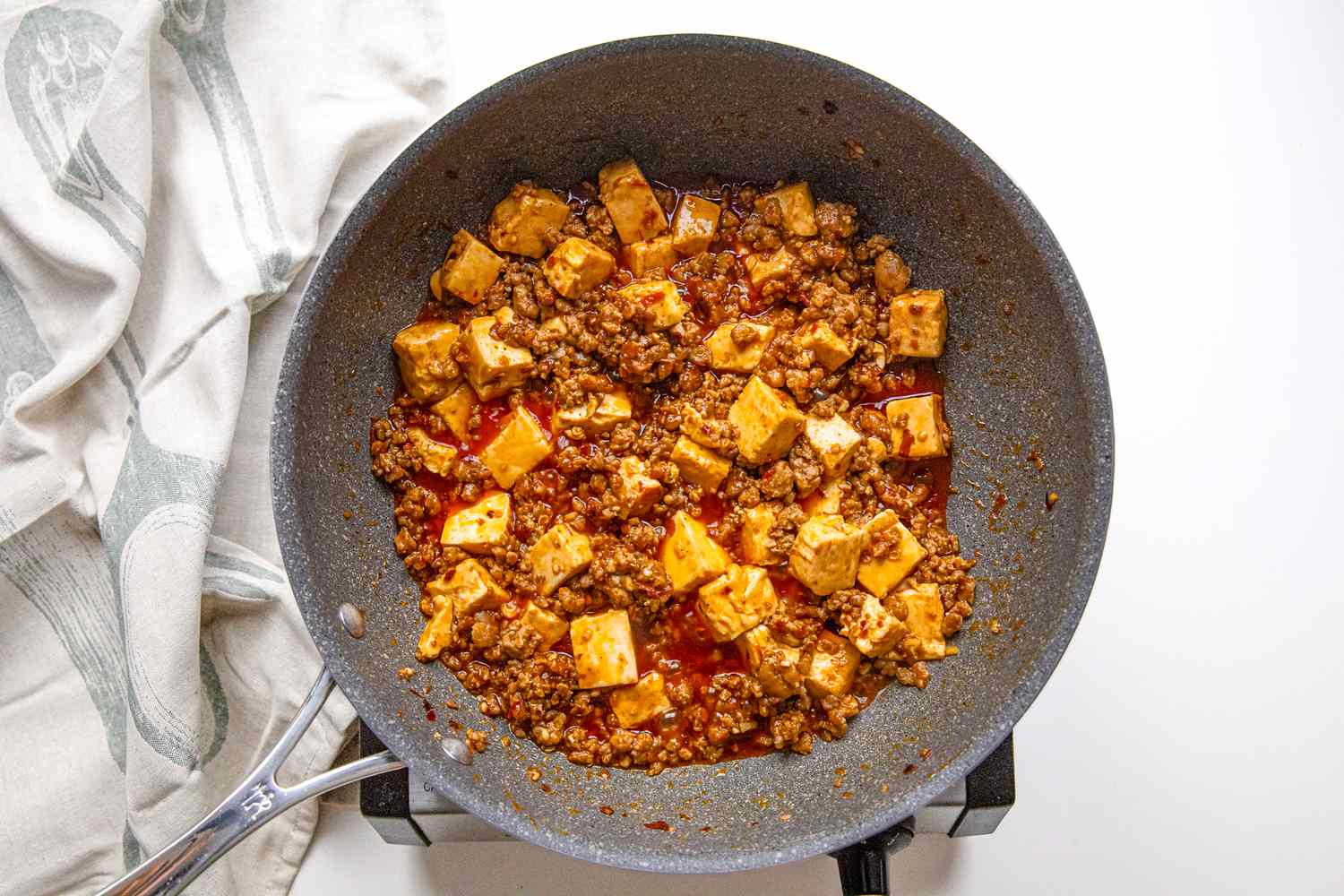 Mapo Tofu in a Pan on a Portable Burner Next to a White Kitchen Towel