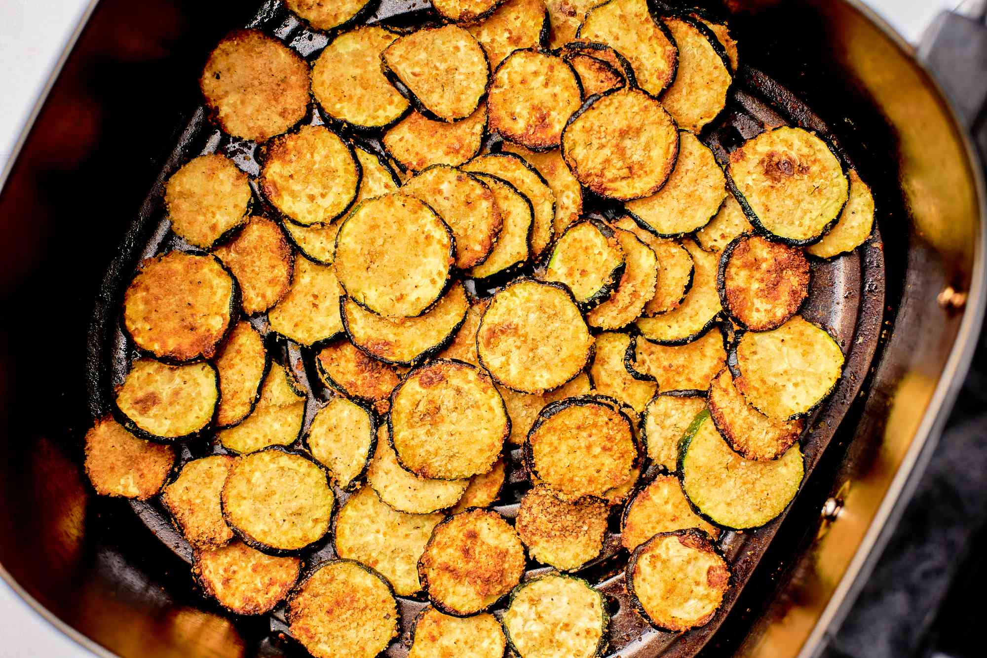 Air fried zucchini slices in the basket of an air fryer