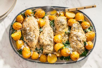 Chicken breasts seasoned and baked with baby potatoes and garnished with herbs and cheese served on a platter