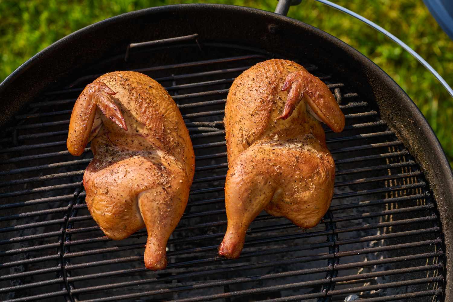 Two grilled half chickens on a barbecue grill