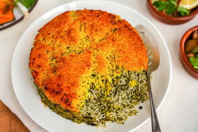 Sabzi Polo (Persian Herb Rice) on a Plate With a Serving Spoon, and Surrounding It, Small Plates With Sides and Glasses of Water 