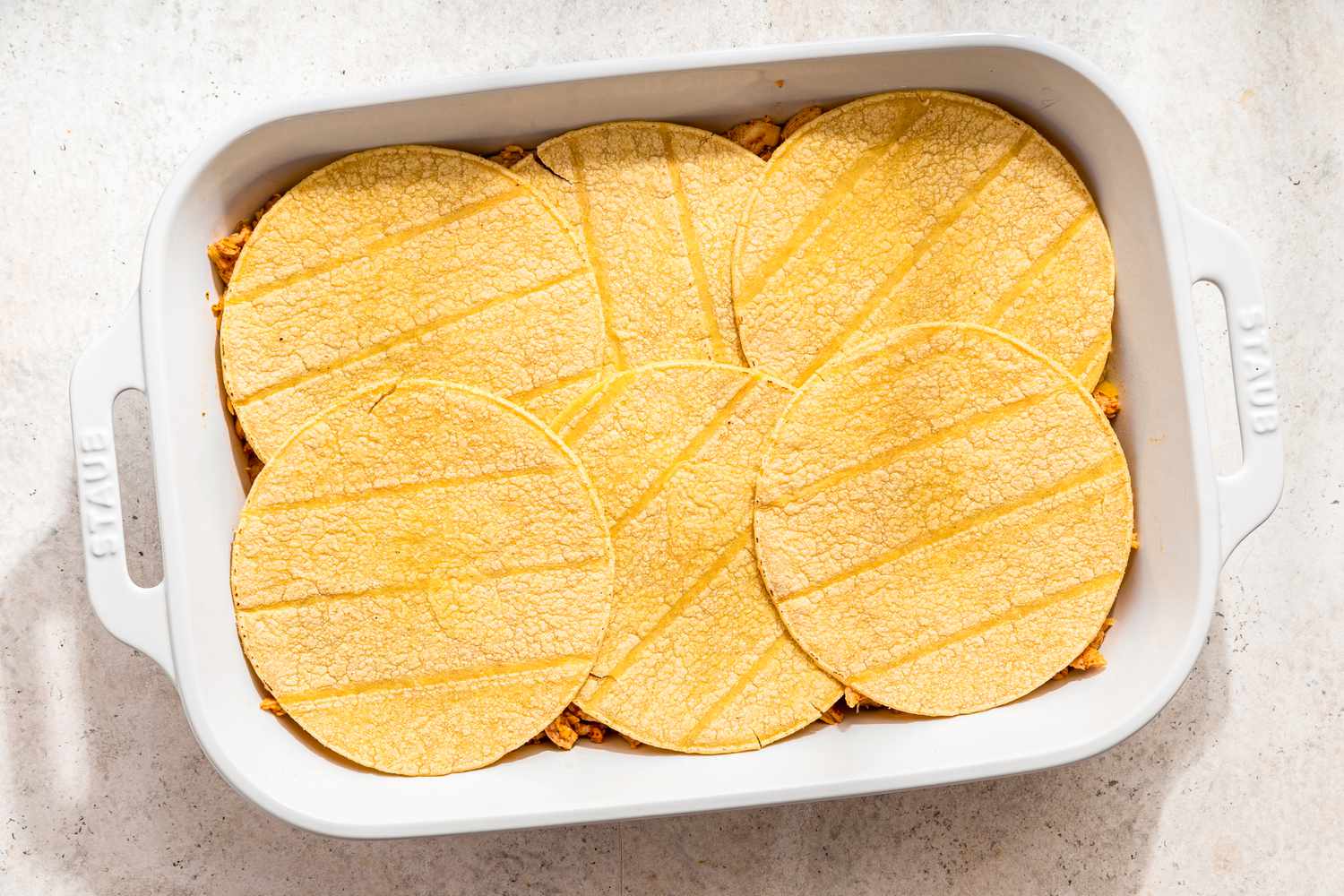 Assembling chicken taco casserole: tortillas added on top of shredded chicken layer