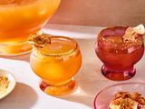 Two glasses of whiskey cider punch garnished with dried apple slices with a punch bowl in the background