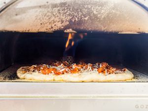 Roccbox pizza oven with a sausage pizza cooking inside. The flame is visible on the inside of the oven.