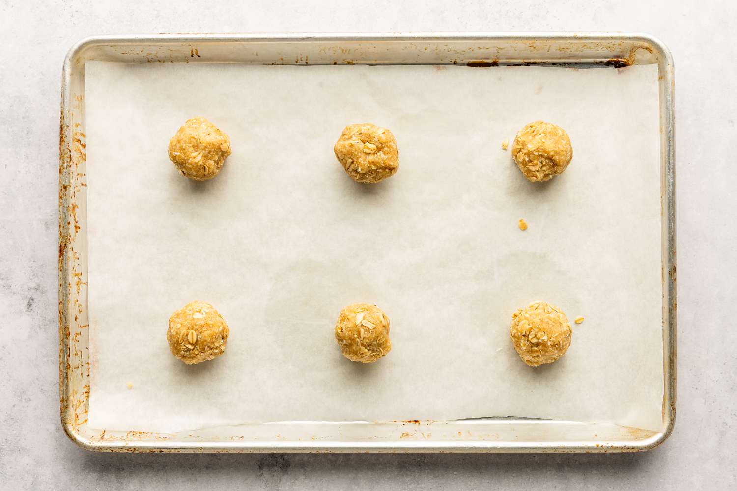 Six dough balls for the Anzac Biscuits recipe placed on a parchment paper lined baking sheet