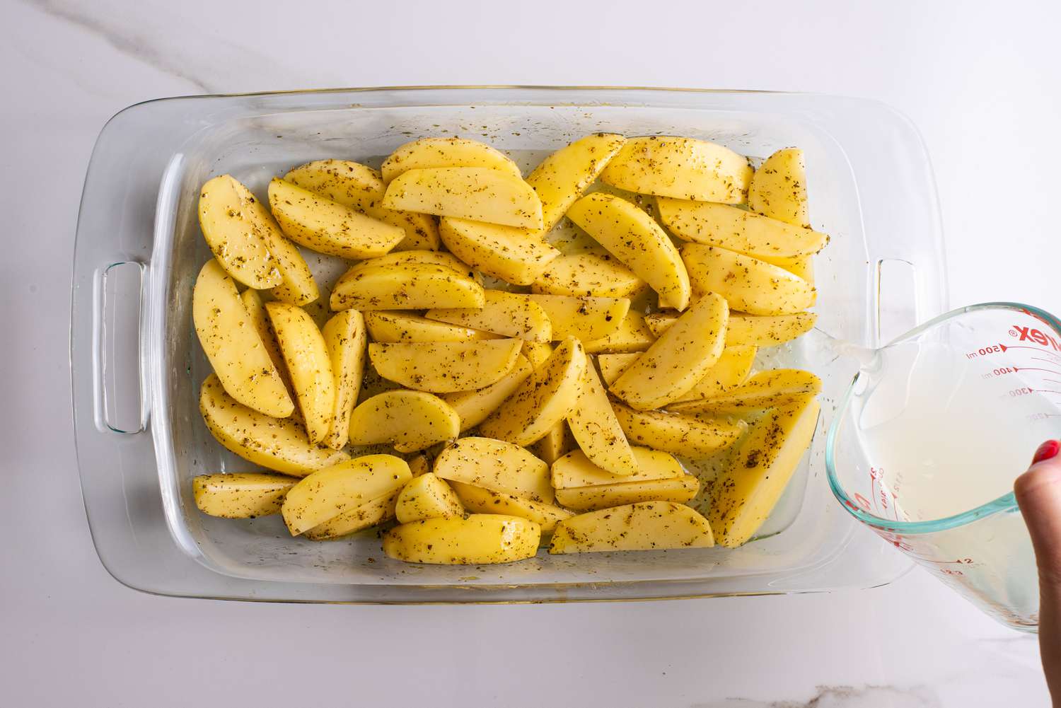 water and lemon juice added to baking pan with uncooked greek lemon potatoes