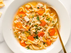 A bowl of chicken noodle soup with carrots noodles and herbs
