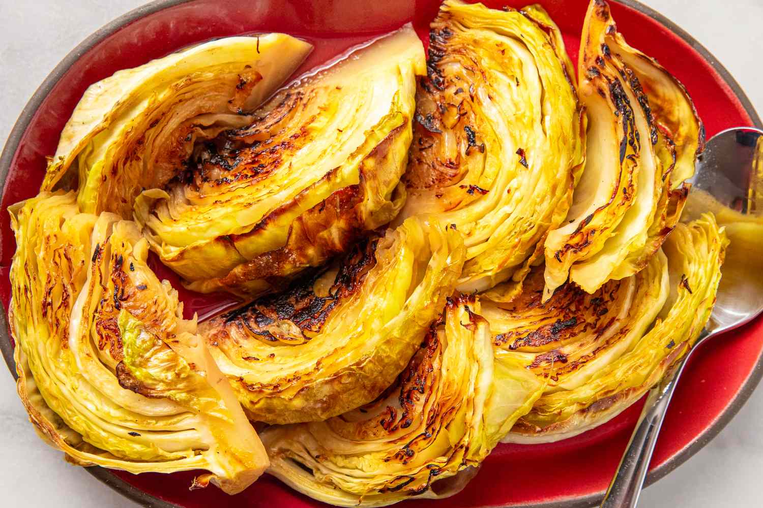Roasted cabbage slices arranged on a red plate with a serving spoon on the side