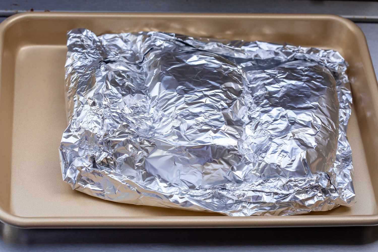 Grilled chicken breast on a baking sheet and covered in foil.