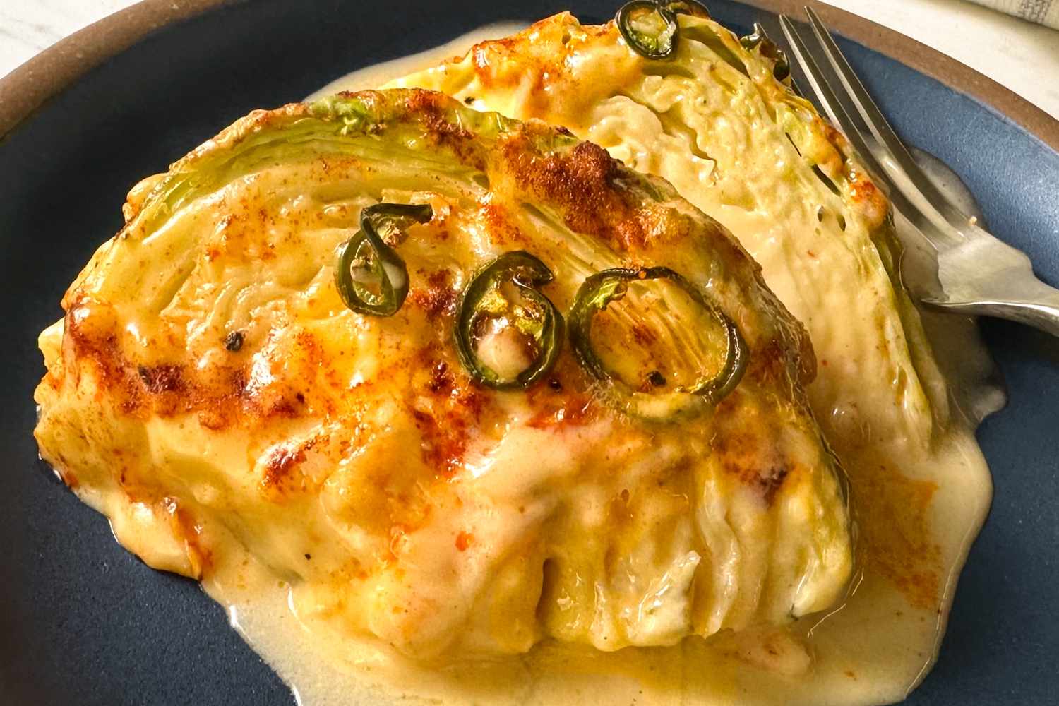 Baked cabbage wedges topped with cheese and sliced jalapeos on a plate