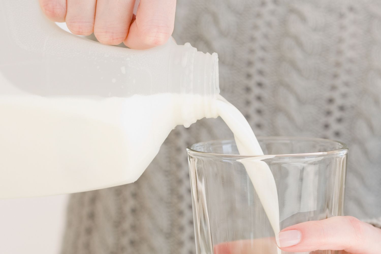 A person pouring milk from a jug into a glass