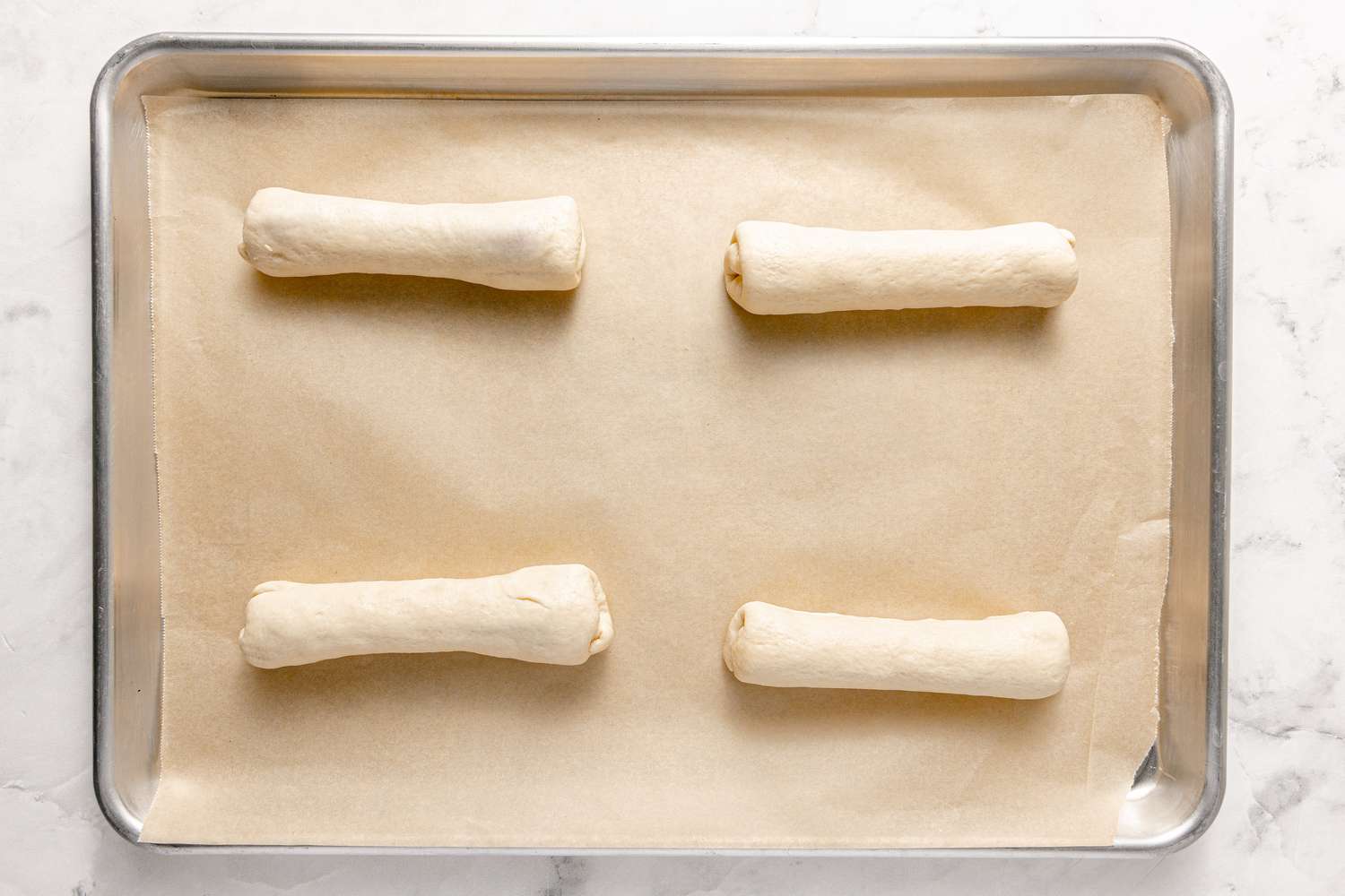 Four Rolled Korean Sausage Ppang on a Lined Baking Sheet