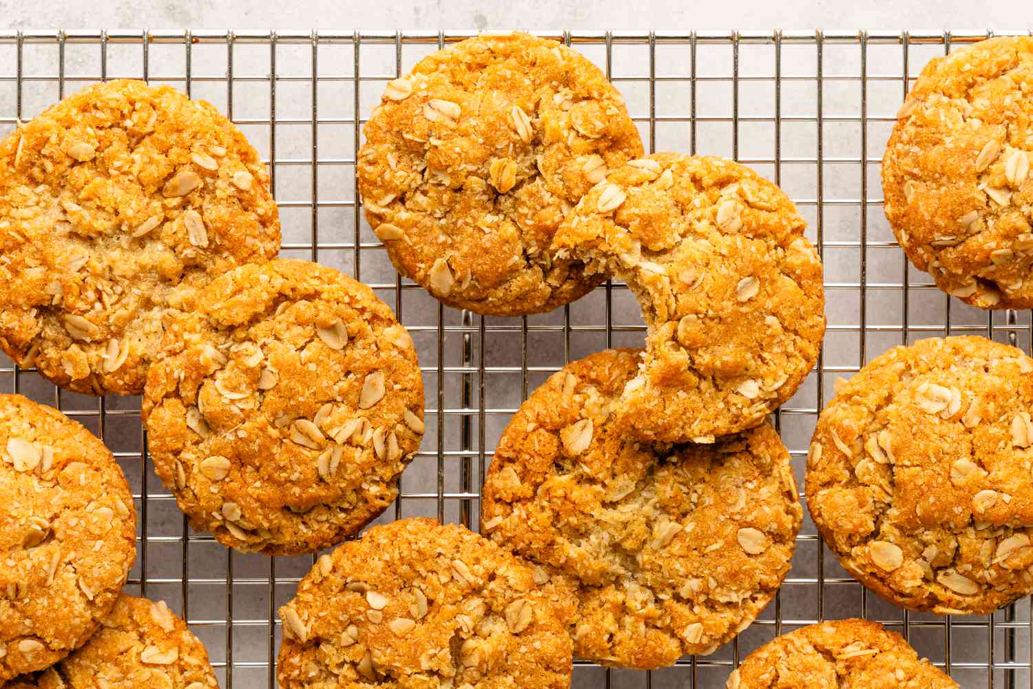 anzac biscuits on a cooling rack, with a bite take out of one of the cookies